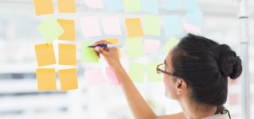 Smiling designer writing on sticky notes on window in creative office-1